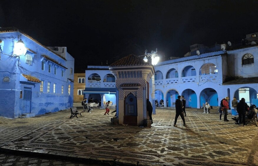 A historic square with blue buildings, a central fountain, and people walking. 4