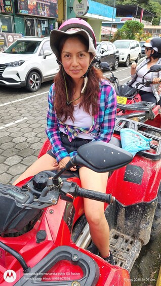 A person sitting on a red ATV with a helmet, in an urban street with cars and buildings. 5