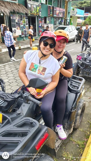 Two people on an ATV, a street with shops, and parked vehicles. 4
