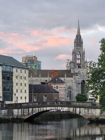 A stone bridge over a river with a church and modern buildings in the background. 2