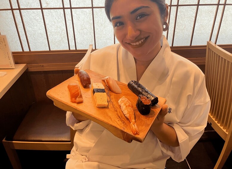 A person holding a wooden tray with various sushi pieces. 1