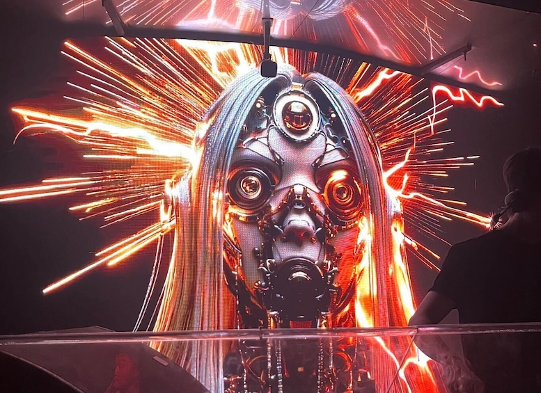 A person standing in front of a large, illuminated digital artwork with a central figure surrounded by dynamic light effects. 4