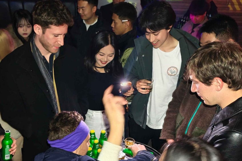 A group of people at a social gathering, some holding drinks and one person taking a photo. 3