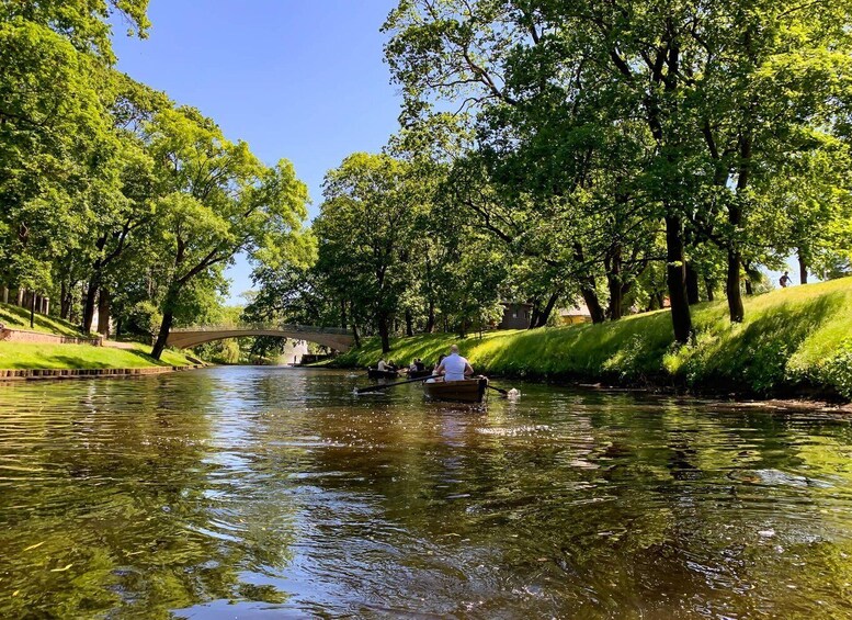 A river with a boat carrying passengers, surrounded by lush green trees and a bridge in the background. 2