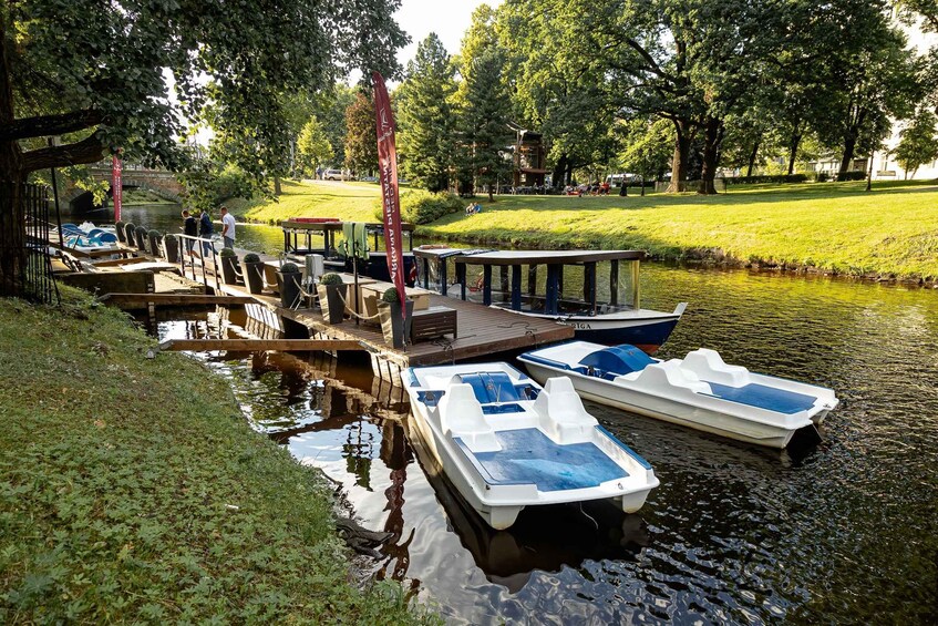 A calm river with boats docked at a wooden pier, surrounded by lush greenery and trees. 1