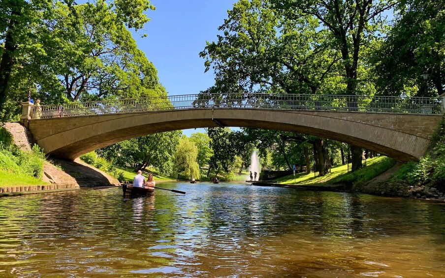 A stone bridge over a river with people rowing boats, surrounded by lush greenery. 4