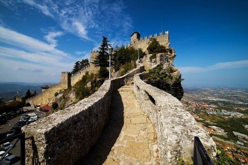 A stone pathway leading to a castle atop a hill with a clear view of the city below. 2