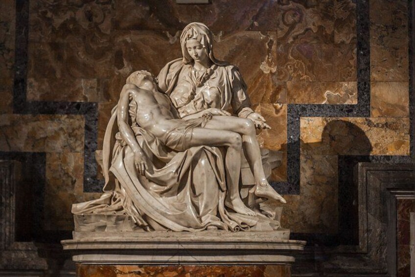 A marble sculpture of a seated figure holding a reclining figure, set against a detailed wall with geometric patterns. 2