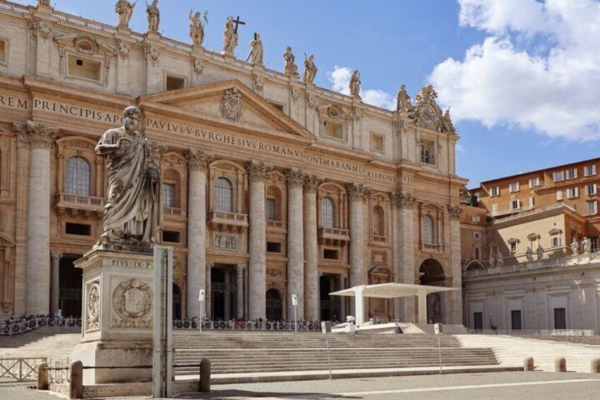 St. Peter's Basilica with a large statue in front, steps leading up to the entrance, and a clear sky. 4