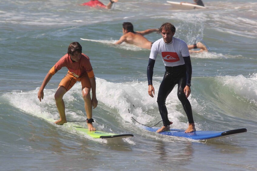 Two surfers on a wave, one in orange and one in white and black. 4