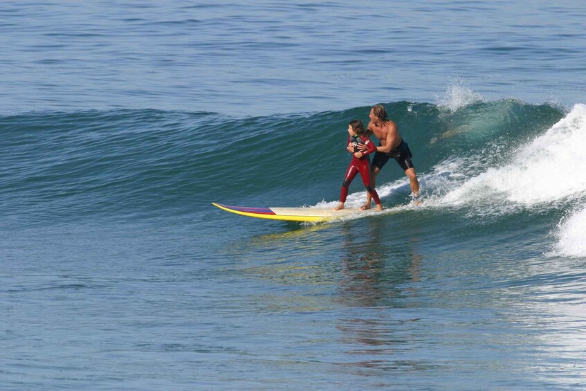 A person surfing on a wave with a child in a red wetsuit. 2