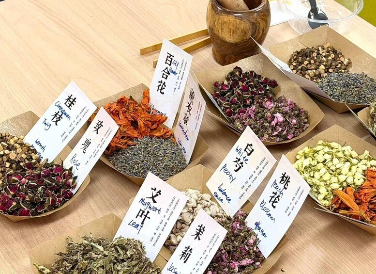 A variety of dried herbs and flowers arranged on a wooden table, each labeled with their names in both English and another script. 1