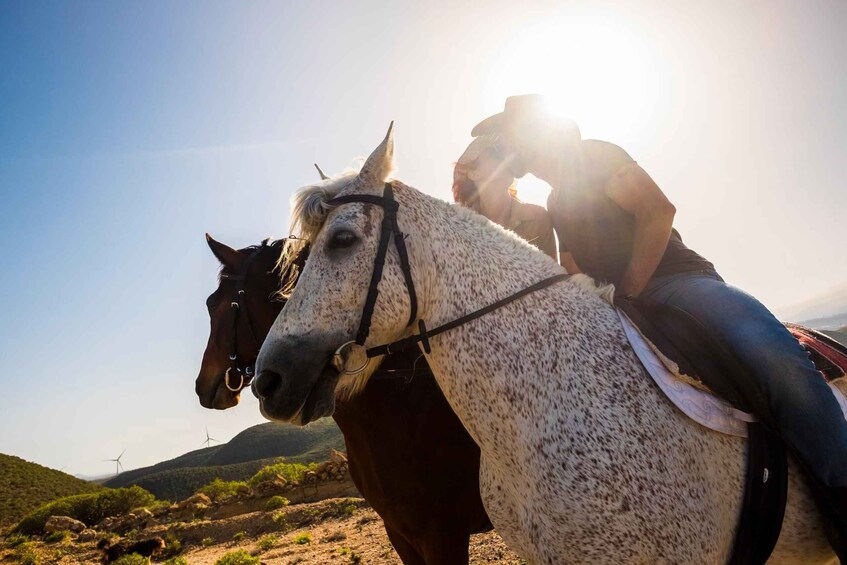 A person riding a white horse with a saddle, in a desert landscape with hills and wind turbines in the background. 3