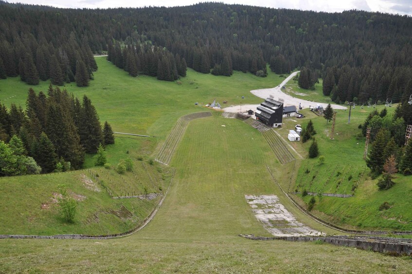 A mountainous landscape with a ski resort, including a chairlift, buildings, and a forested area. 1