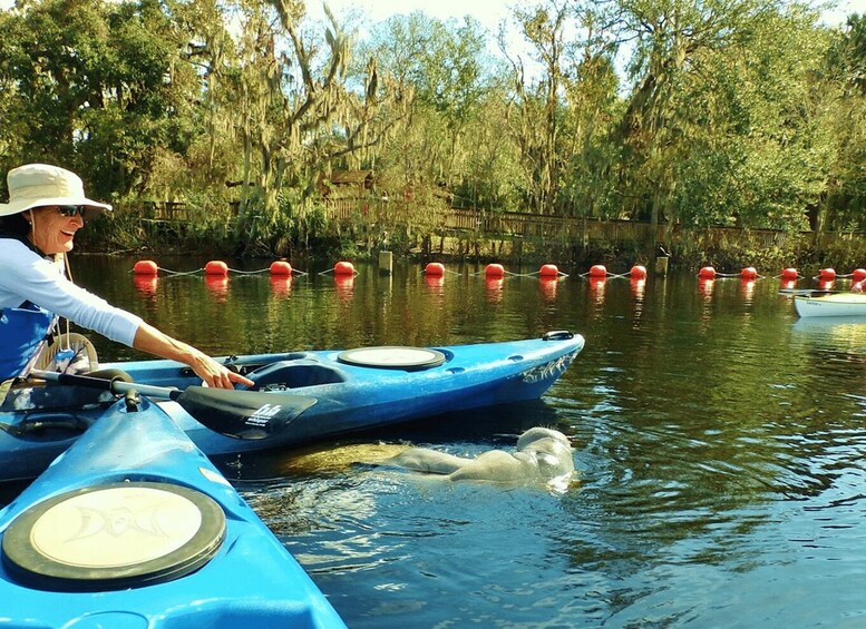 A person in a blue kayak on a calm river with trees and red buoys in the background. 2