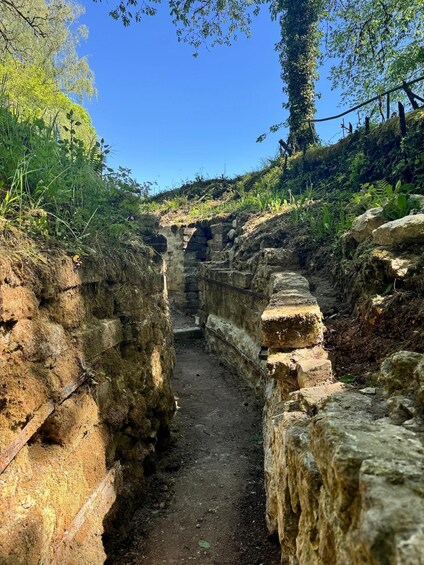A narrow stone pathway flanked by walls, leading to an arched structure in a lush, green environment. 3