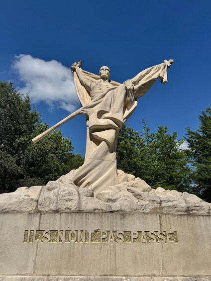 A statue of a figure with outstretched arms, standing on a pedestal with inscriptions. 1
