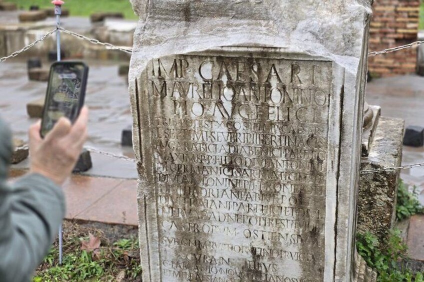 A gravestone with inscriptions, surrounded by a metal fence, with a person taking a photo. 5