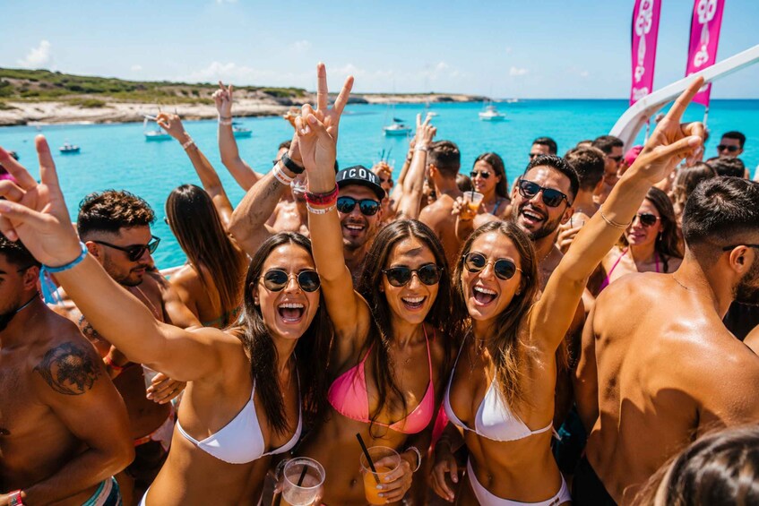 A group of people at a beach party with a clear blue sea and boats in the background. 1