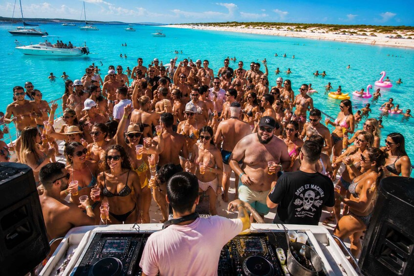 A crowded beach with people swimming and socializing, boats in the water, and a DJ booth on a boat. 1