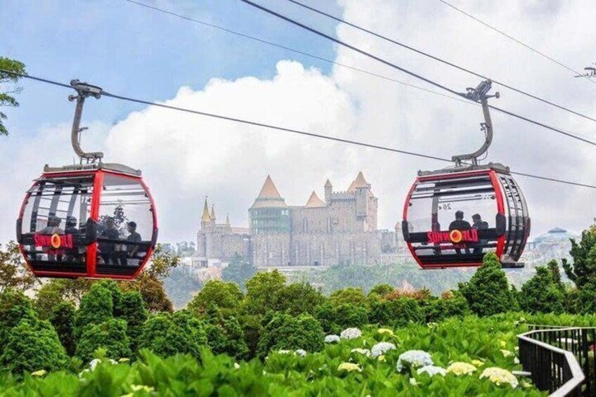 Two cable cars with passengers, a castle-like building in the background, and lush greenery in the foreground. 5