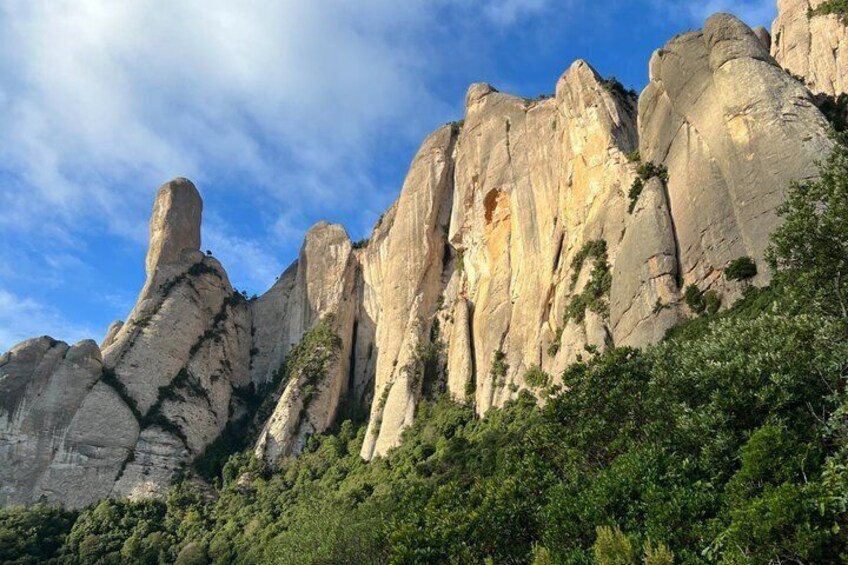 A rugged mountain range with prominent rock formations and dense green foliage at the base. 1