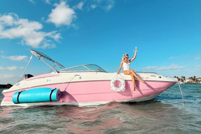 A pink speedboat with a person on board, a life preserver, and calm water. 1