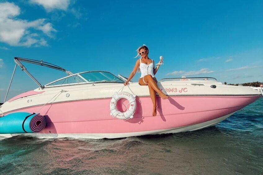 A pink and white boat with a person sitting on the deck, a life ring, and the registration number '3943 JC' on the side. 3