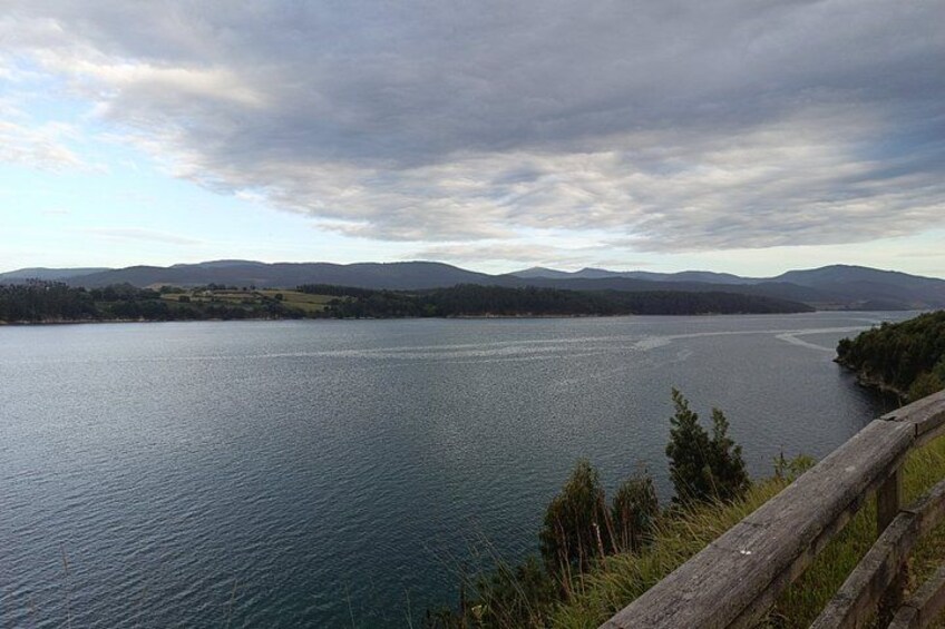 A large body of water with a wooden fence in the foreground, surrounded by hills and a cloudy sky. 2