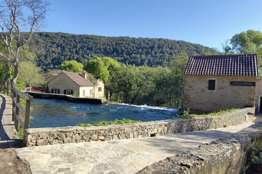 A stone bridge over a river, a house with a tiled roof, and a forested hillside in the background. 3