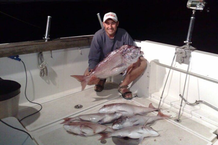 A person holding a large fish on a boat with several smaller fish on the deck. 3