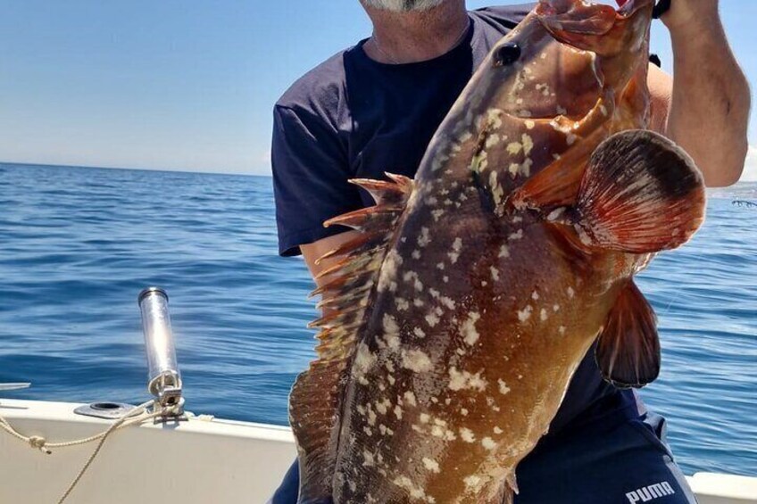 A person holding a large fish with white spots, on a boat in the ocean. 1