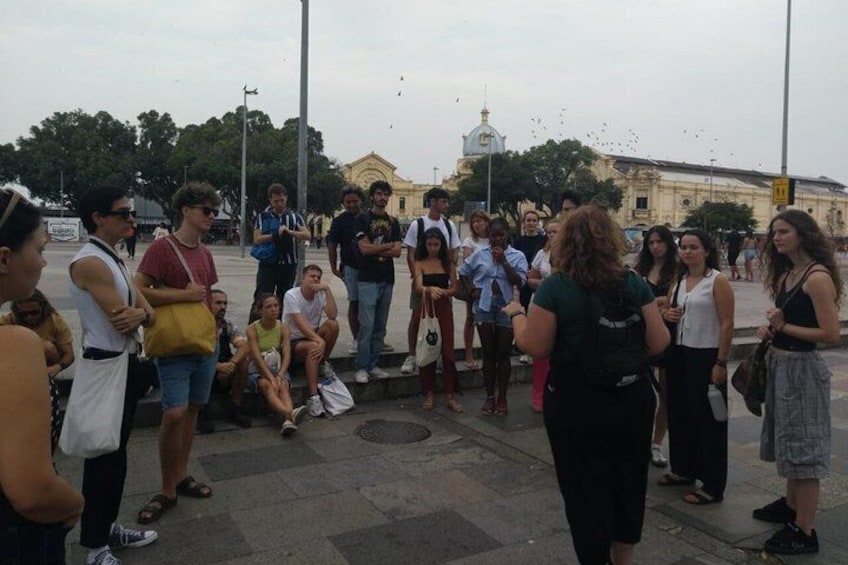 A group of people standing and sitting on a city square with buildings and a dome in the background. 2