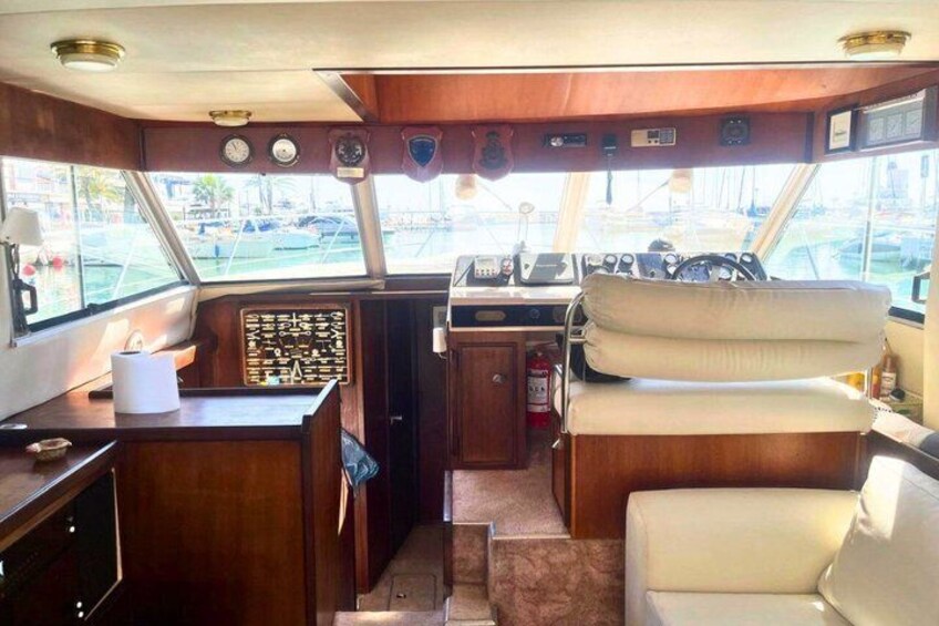 A boat's interior with a steering wheel, control panel, and cushioned seating. 4