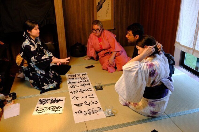 A group of people in traditional Japanese attire sitting on tatami mats, with calligraphy and paper scrolls on the floor. 4