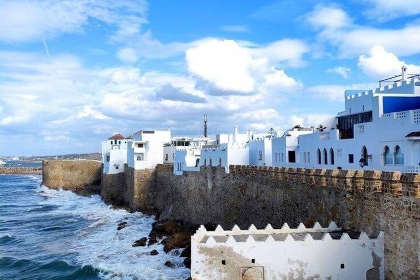 A coastal town with white buildings, a stone wall, and the sea. 1