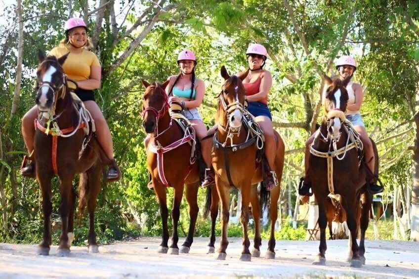 Three people riding horses on a dirt path with trees in the background. 1