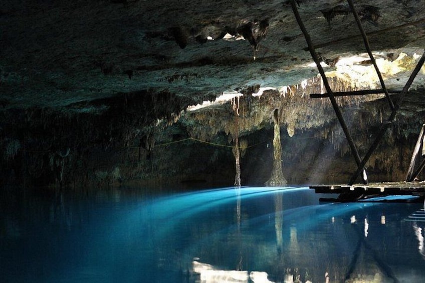 A cave with a blue pool, stalactites, and a metal structure. 5