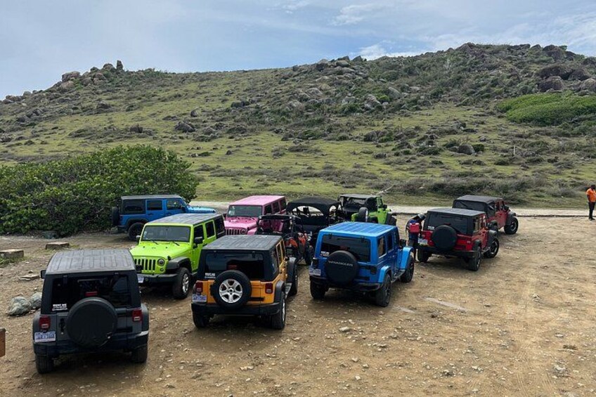A group of off-road vehicles parked on a dirt road with a hilly landscape in the background. 2