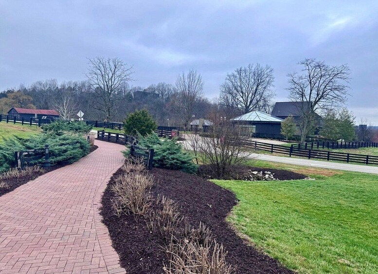 A brick pathway leading through a park with green grass, trees, and a building with a green roof. 3