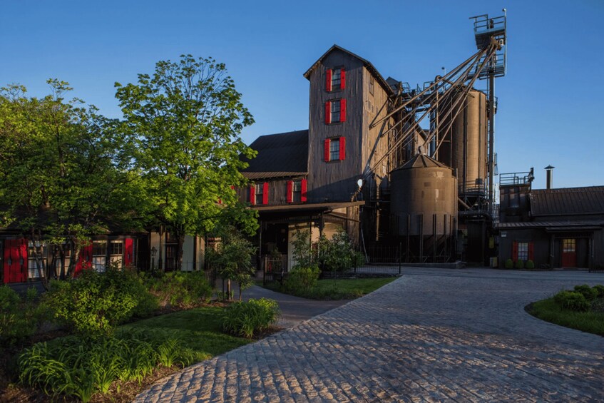A historic industrial building with red shutters, a cobblestone pathway, and lush greenery. 1