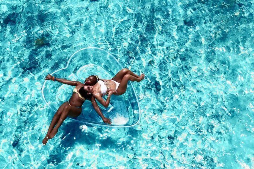 Two people floating on a clear blue pool with a heart-shaped float. 4