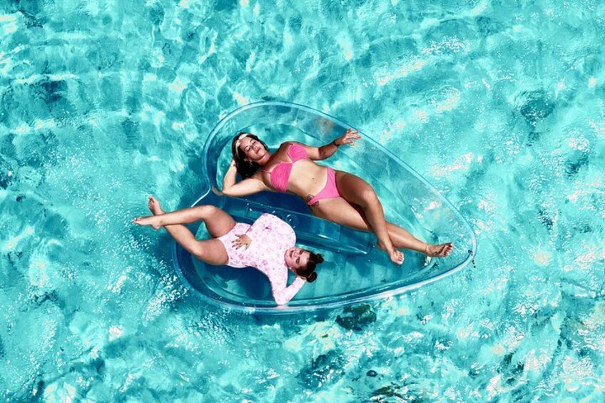 Two people floating on a clear blue inflatable raft in a swimming pool. 5