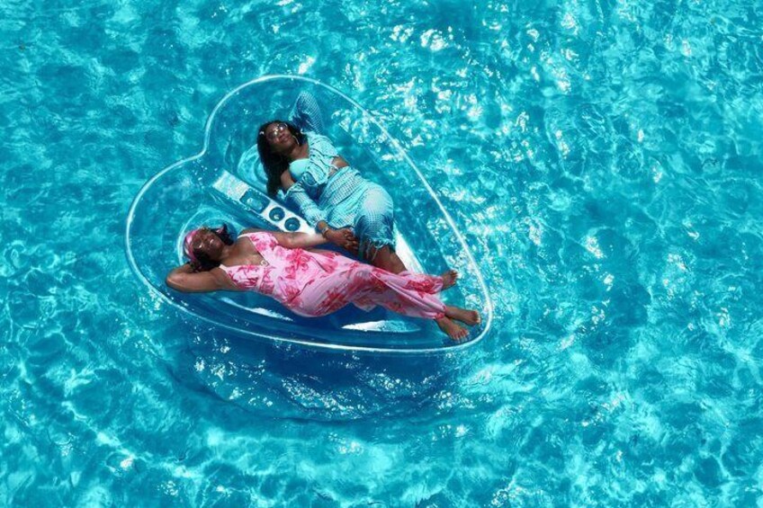 Two people floating in a heart-shaped inflatable pool in a clear blue pool. 1