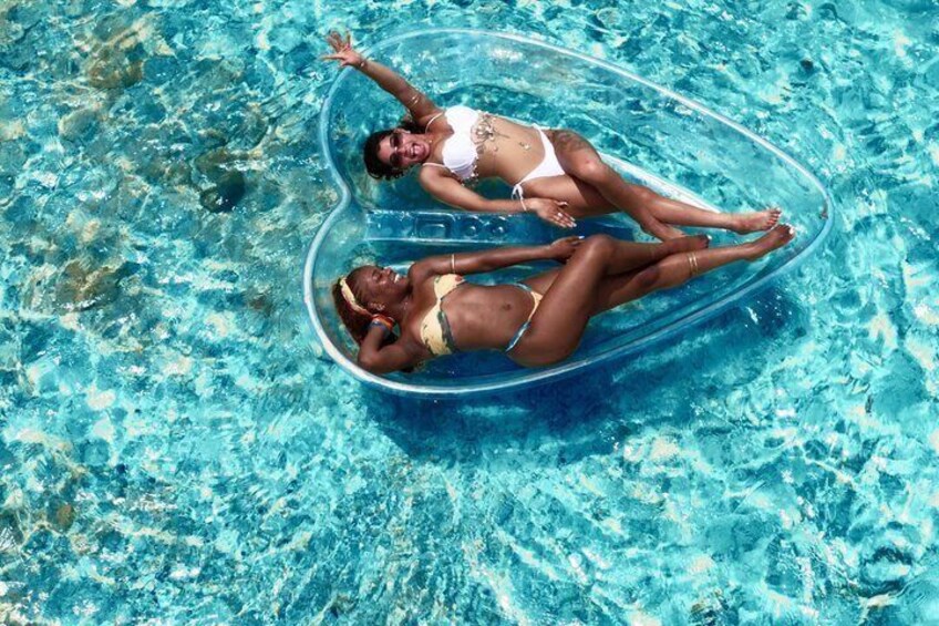 Two people floating in a heart-shaped inflatable pool in a clear blue pool. 3