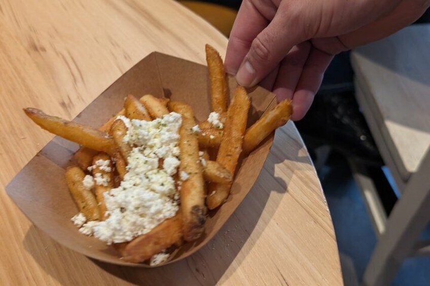A hand holding a piece of French fries topped with cheese. 3