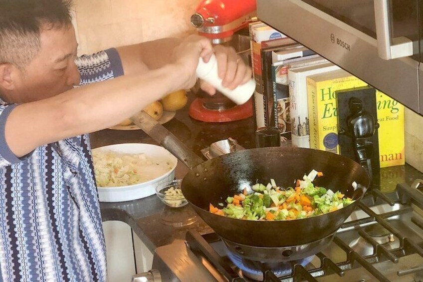 A person cooking vegetables in a wok on a stove. 2