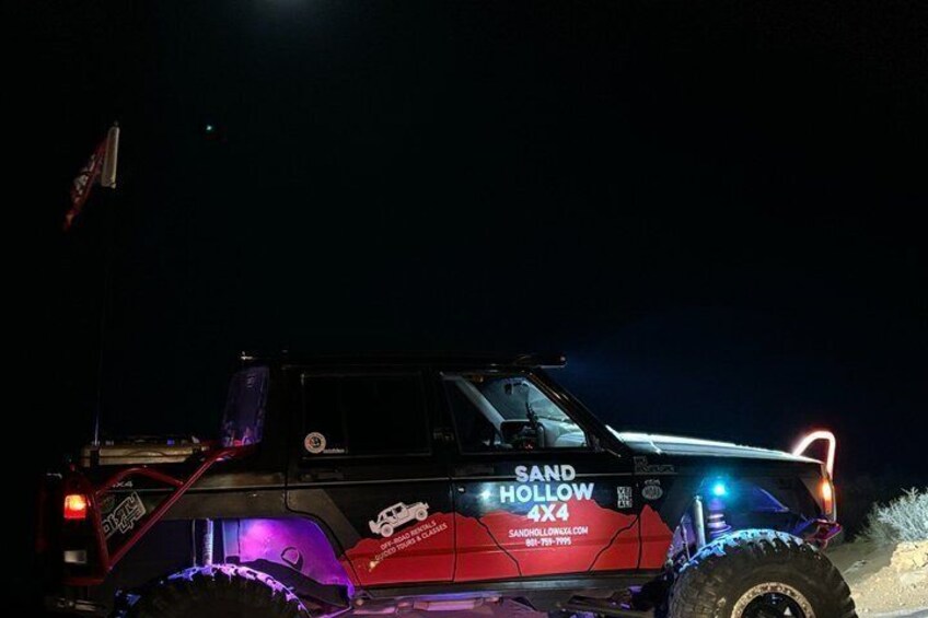 A red off-road vehicle with 'SAND HOLLOW 4X4' written on the side, parked at night. 2