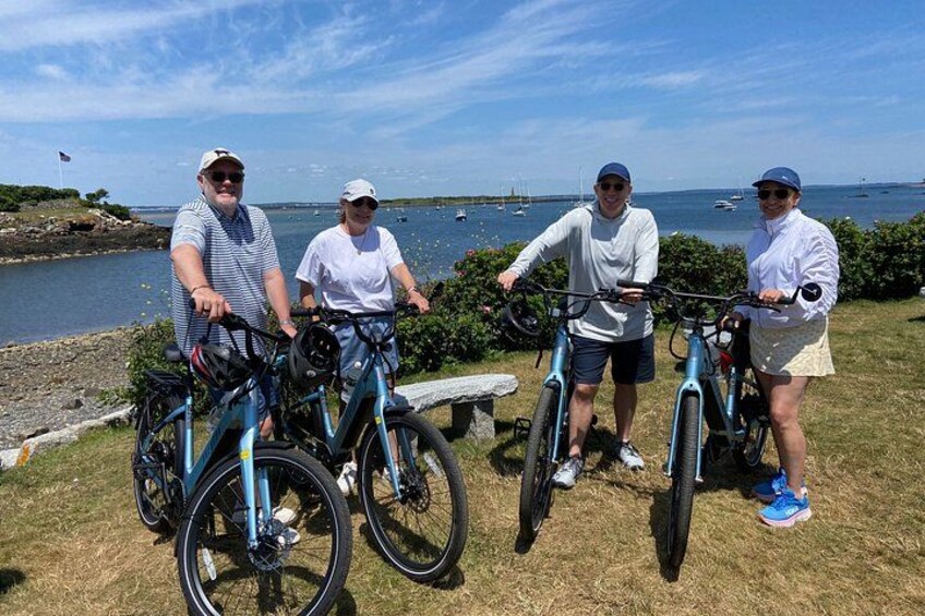Four people standing on grass near a body of water with bicycles. 4