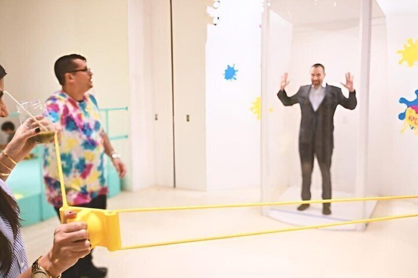 A person in a suit inside a transparent enclosure with yellow lines, surrounded by colorful wall decorations. 1
